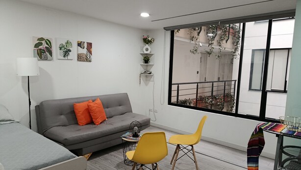 Ein modernes Wohnzimmer mit einem grauen Sofa, orangefarbenen Kissen, einem Couchtisch und zwei gelben Sessel.