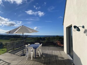 A wooden deck with a table and chairs, an umbrella, and a view of the landscape. - Charming House in Landeda With Sea View (Landeda)