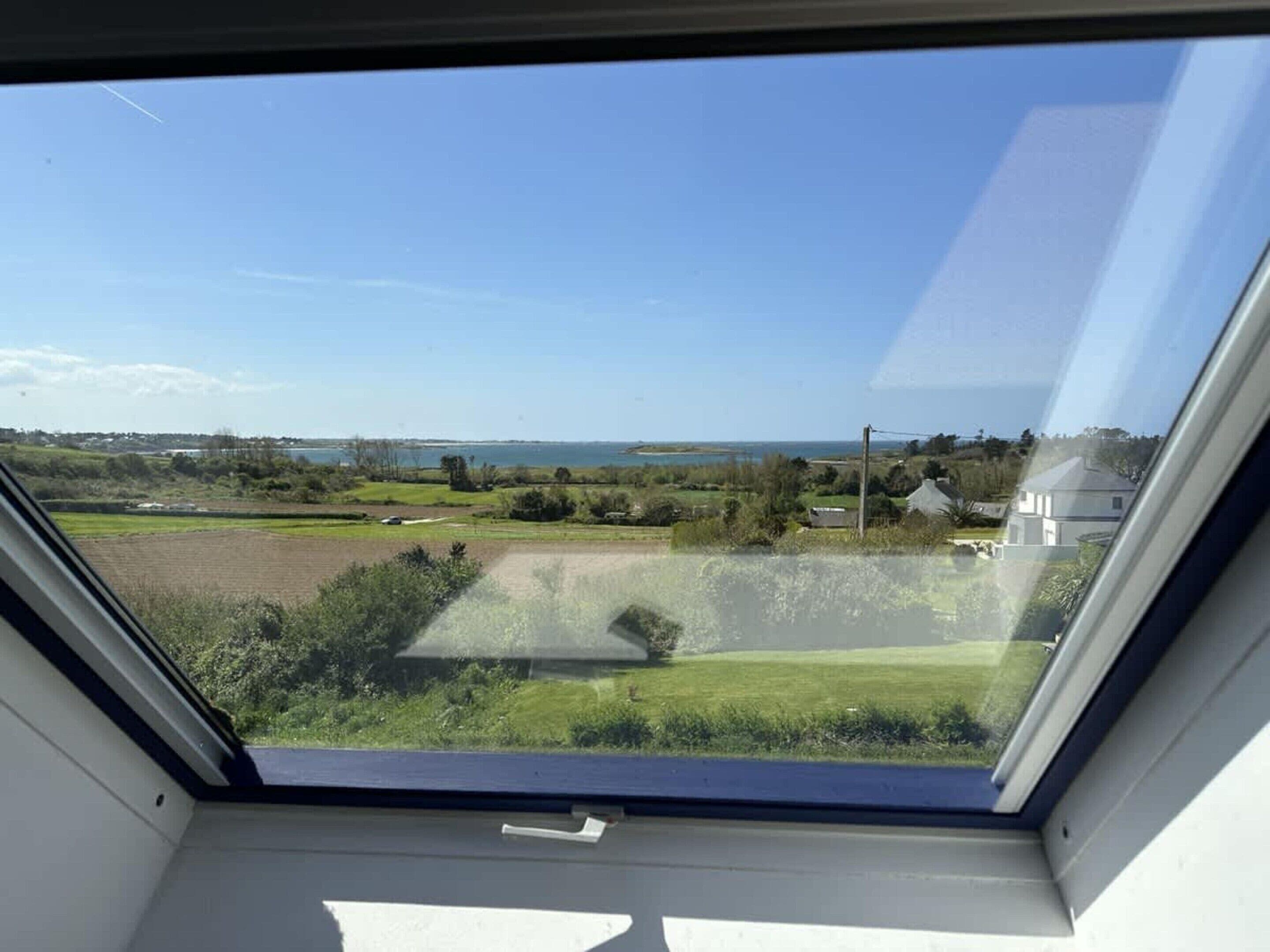 Ein Oberlichtfenster mit Blick auf eine grüne Landschaft, ein Gewässer und entfernte Gebäude.