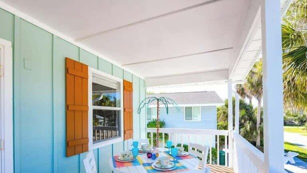 Eine überdachte Veranda mit Esstisch, weißen Stühlen und einem Fenster mit Fensterläden.