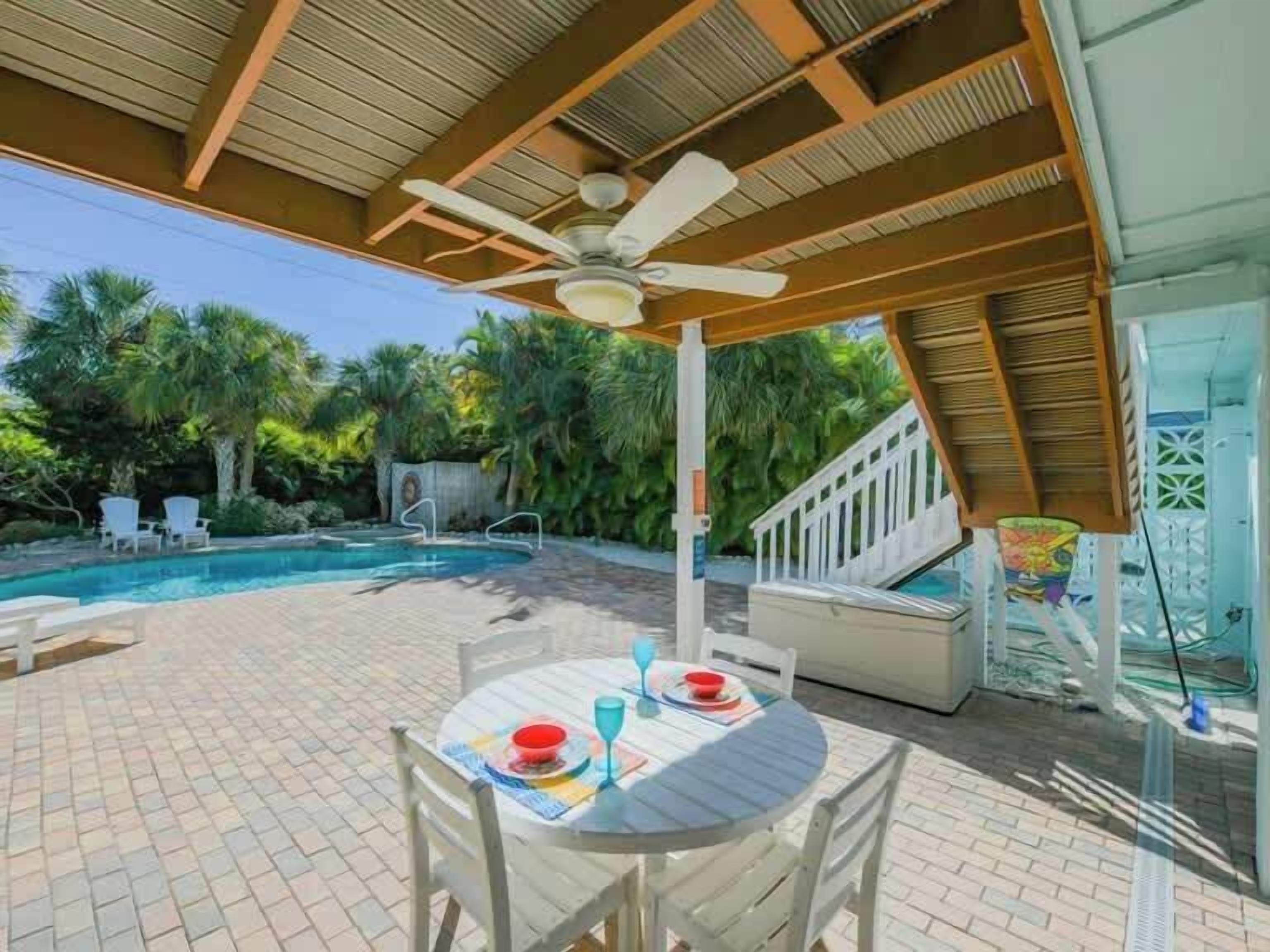 An outdoor pool area with a covered patio, a table with chairs, and a staircase leading to a deck.
