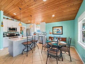 A kitchen with a central island, bar stools, and a dining table with chairs.