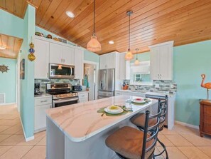 A kitchen with white cabinets, a central island, and a dining area with bar stools.