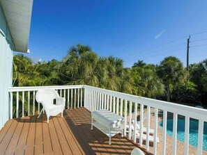 A wooden deck with white railings, a pool, and palm trees in the background.