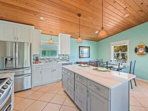 A modern kitchen with a large island, stainless steel appliances, and a wooden ceiling.