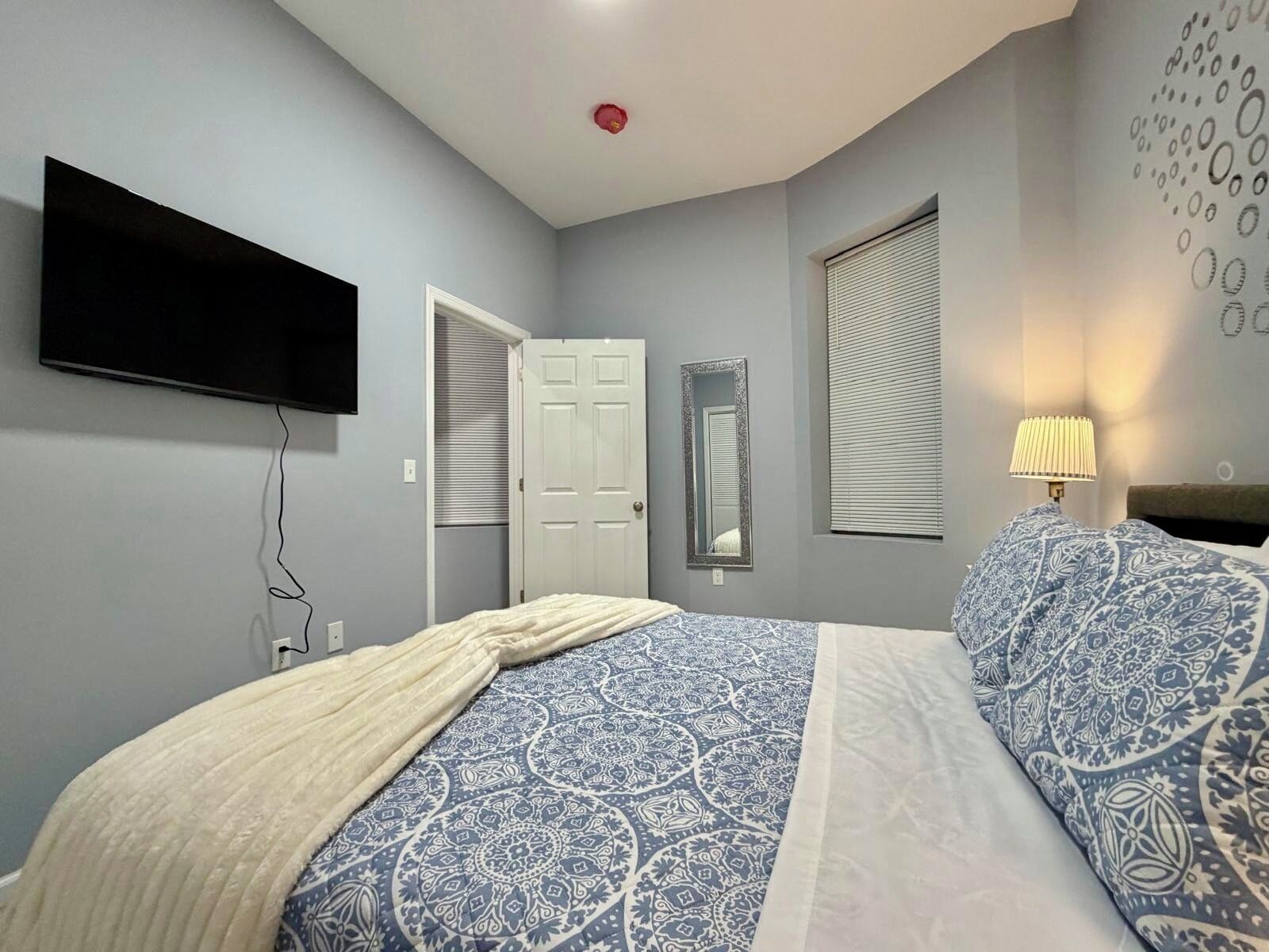 Een slaapkamer met een bed, een televisie, een deur, een raam en een spiegel bevestigd aan de muur.