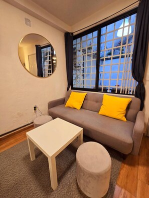 Ein Wohnzimmer mit einer Couch, einem runden Spiegel, einem kleinen Tisch und einem Fenster mit Blick.