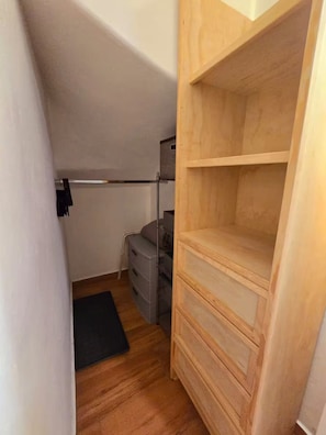Ein kleines Zimmer mit einem Holzschrank, einem Metallgestell und einer grauen Kommode.