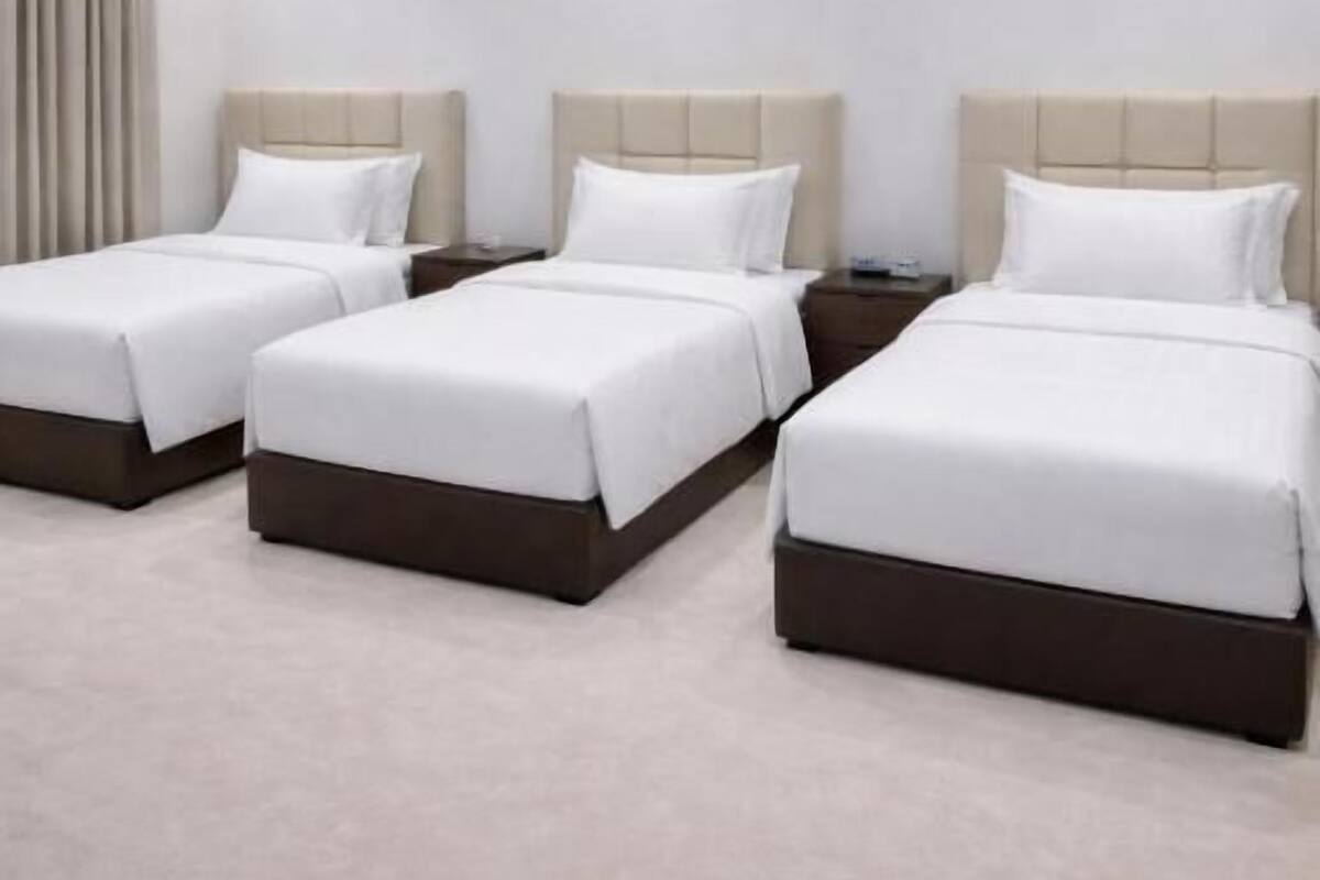 Habitación de hotel con tres camas, una lámpara en el techo y piso alfombrado.