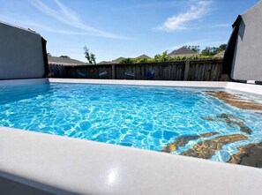 A swimming pool with clear blue water, surrounded by a wooden fence and a clear sky. - NMB Compound-2 Homes-6BR 6BA-Pool HotTub-Sleeps 22 (North Myrtle Beach)