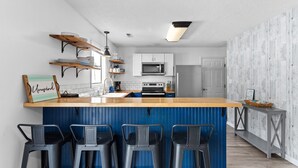 Une cuisine moderne avec un coin bar, des meubles blancs, un four à micro-ondes et un mur d’accent bleu.