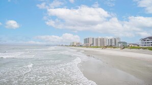 Une plage avec des vagues, une étendue de sable et des bâtiments en arrière-plan.