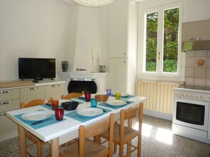 A kitchen with a dining table set for four, a television, a fireplace, and a window with a view of greenery. - Holiday Home 'Cascinetta' with Mountain View, Private Garden and Wi-Fi (Castello)