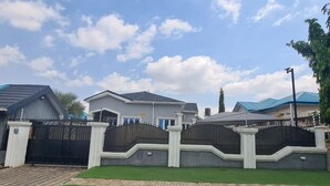 A gated residential area with houses, a paved driveway, and a well-maintained lawn.