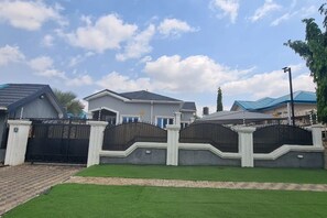 Área residencial murada com casas, entrada pavimentada e gramado bem cuidado.
