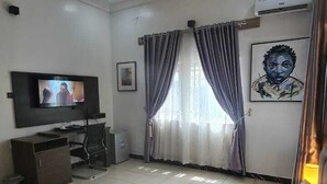 A hotel room with a bed, a desk, a television, an air conditioner, and a window with curtains.