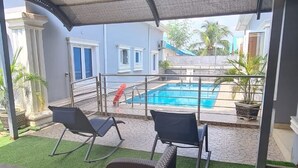 A covered outdoor area with a pool, two rocking chairs, and a small table.