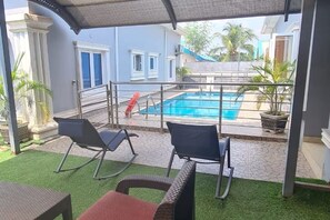 A covered outdoor area with a pool, two rocking chairs, and a small table.