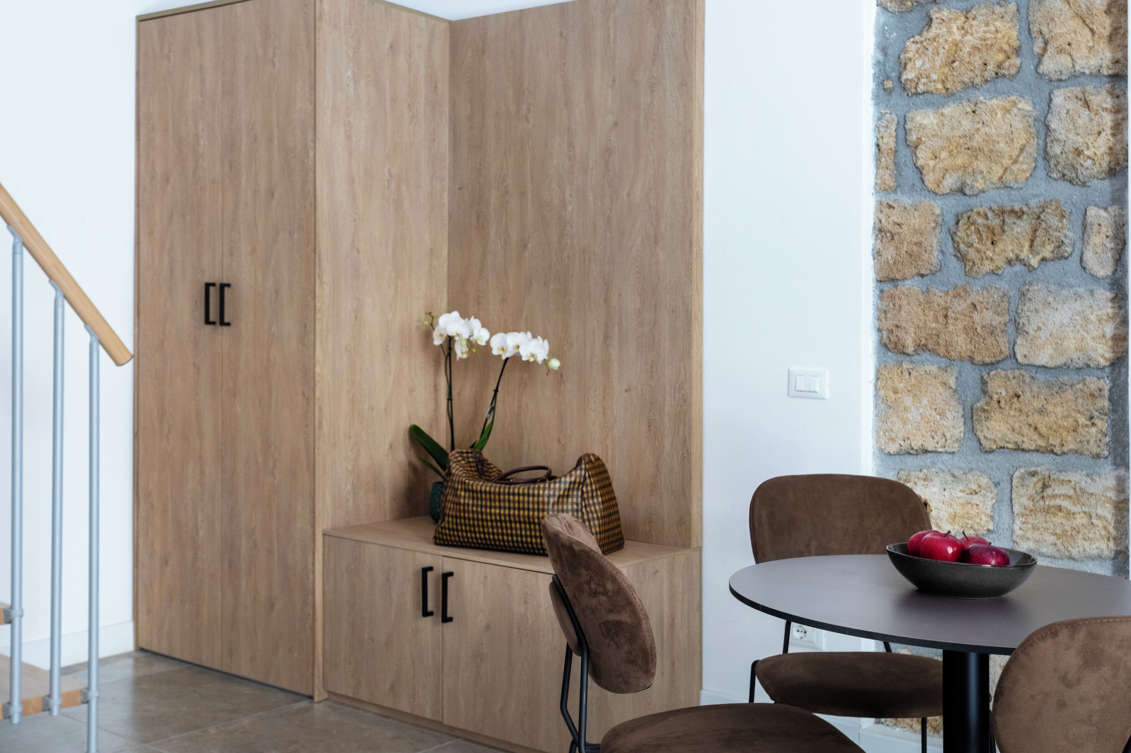 A room with a wooden wardrobe, a table with chairs, and a stone wall.