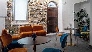 Un interior moderno con pared de piedra, puerta de madera y sillas naranjas y azules alrededor de una mesa redonda.