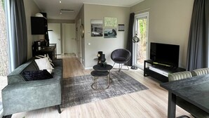 A modern living room with a sofa, a chair, a TV, and a dining table. - Just Nature Light 4 (Arnhem)