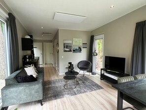 A modern living room with a sofa, a chair, a TV, and a dining table. - Just Nature Light 4 (Arnhem)
