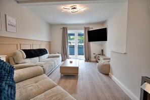 Ein modernes Hotelzimmer mit Sofa, kleinem Tisch, Fernseher und einer Schiebeglasdoor zum Außenbereich.