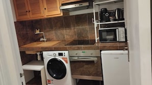 Eine kompakte Küche mit Holzausstattung, einer Waschmaschine, einer Mikrowelle und einer Kaffeemaschine.