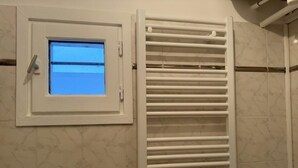 Ein Badezimmer mit weiß gefliester Wand, einem Fenster mit Blick auf Blau und einem weißen Handtuchhalter.