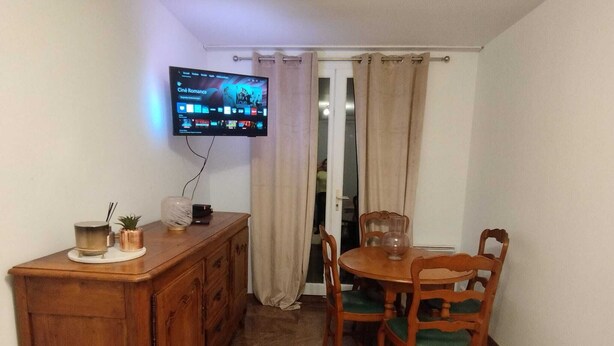 Ein kleiner Essbereich mit Holztisch und Stühlen, einem an der Wand befestigten Fernseher und einem Schrank mit diversen Gegenständen darauf.