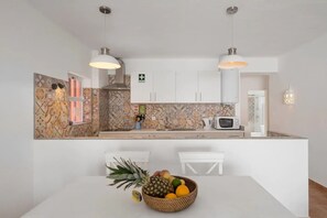 Une cuisine moderne avec des meubles blancs, un four à micro-ondes et un panier de fruits posé sur le plan de travail.