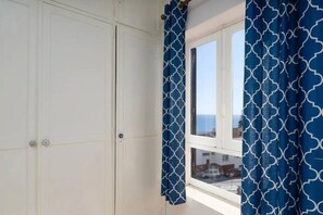 Une pièce avec une fenêtre, une armoire blanche et des rideaux bleus à motifs.