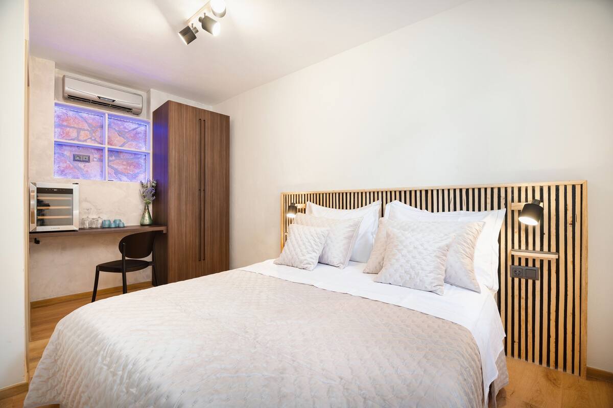 Un dormitorio con una cama grande, un cabecero de madera, un escritorio con una silla y un equipo de aire acondicionado.