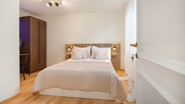 A bedroom with a bed, wooden headboard, bedside tables, and a desk with a chair. - Hygge Rooms Split (Split)