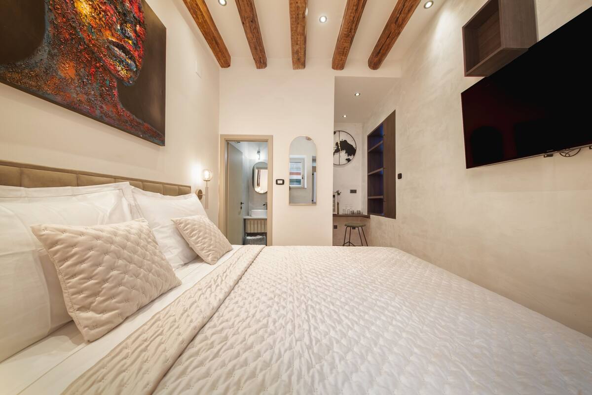 Un dormitorio con una cama grande, un cuadro en la pared y un televisor fijado a la pared.