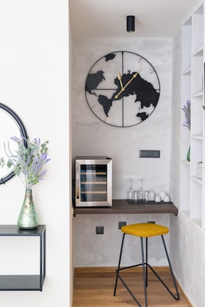 Eine moderne Küche mit einer runden Wanduhr, einem Edelstahlkühlschrank, einem gelben Hocker und einer Vase mit Blumen.