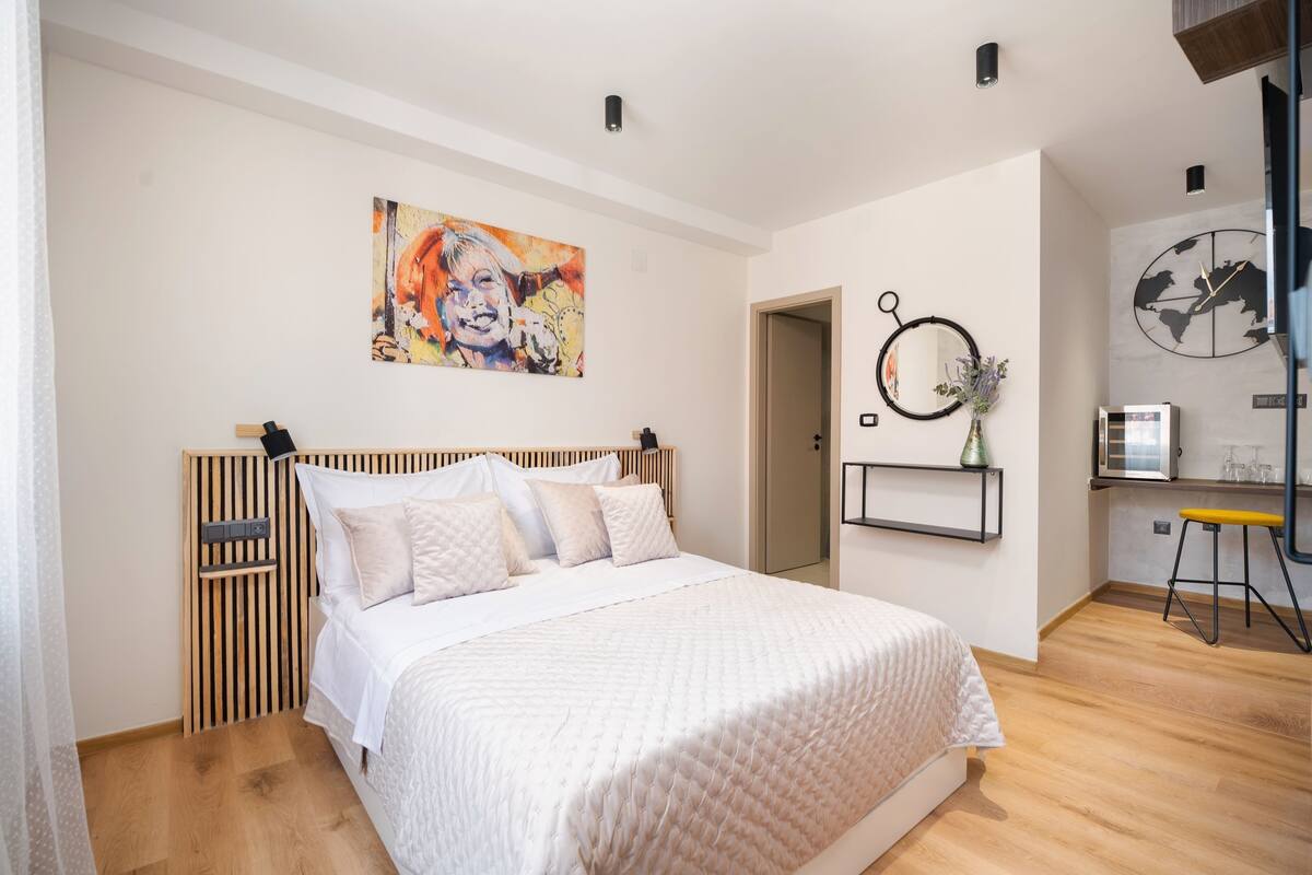 Un dormitorio con una cama, un cuadro, un reloj y un pequeño escritorio con una silla.