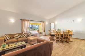 A living room with a sofa, coffee table, and dining area with wooden chairs and a table. - Villa Dean: Private Pool | For Families | AC & WI- (Lagos)