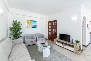 A living room with a sofa, two armchairs, a coffee table, a TV on a wooden stand, a painting on the wall, and a potted plant. - Moinhos: Location | Pool | Families and Couples (Lagos)