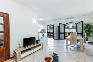 A modern living room with a TV, a dining table, and a kitchen in the background. - Moinhos: Location | Pool | Families and Couples (Lagos)