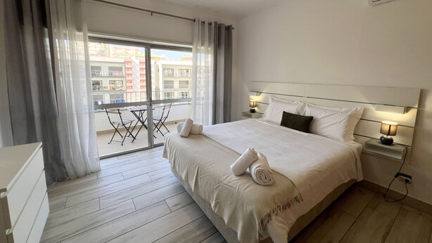 Habitació d'hotel amb llit, escriptori, cadira, balcó amb taula i cadires, i aire condicionat.