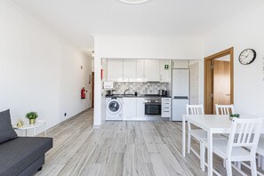 Eine moderne Küche mit weißen Schränken, einer Waschmaschine und einer Essecke mit weißen Stühlen und einem Tisch.