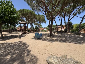 Ein Spielplatz mit Rutsche, Schaukeln und einer großen dekorativen Skulptur.