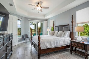 A bedroom with a four-poster bed, a ceiling fan, a nightstand, a dresser, and a window with a view of greenery. - SWEETWATER BAY - Waterfront Cape Coral Pool house 3/2 fenced yard, kayaks, bikes (Cape Coral)