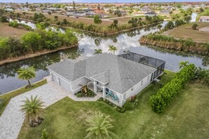 A two-story house with a covered patio, a pond, and a well-maintained lawn. - SWEETWATER BAY - Waterfront Cape Coral Pool house 3/2 fenced yard, kayaks, bikes (Cape Coral)