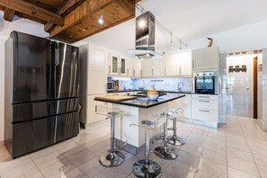 A modern kitchen with stainless steel appliances, a central island with stools, and wooden ceiling beams. - Moradia de Silves | Nature Retreat (Silves)