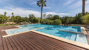 Ein Schwimmbad mit Holzterrasse, umgeben von Palmen und Grünpflanzen.