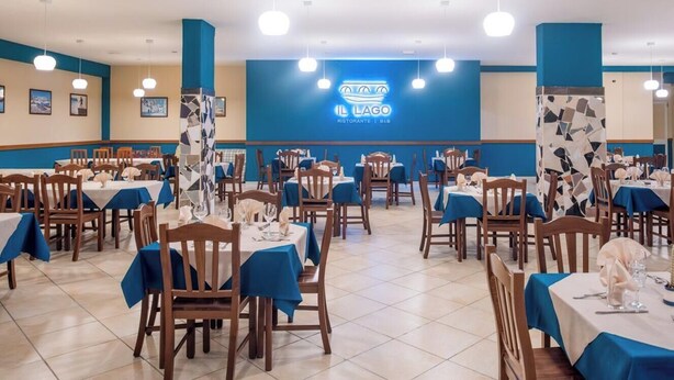 Um restaurante com várias mesas e cadeiras, esquema de cores azul e branco, e um logotipo na parede.