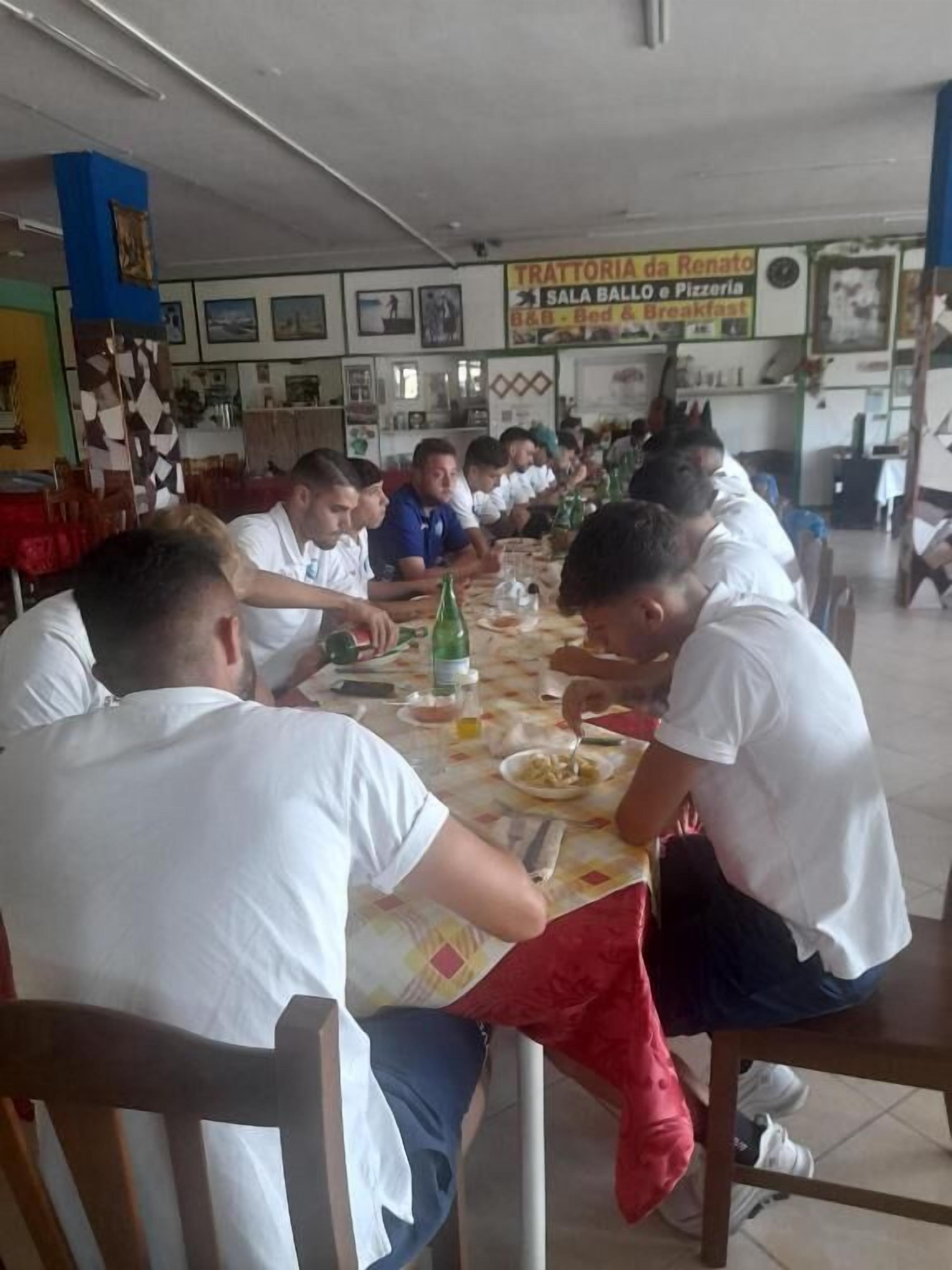 A group of people seated around a table in a dining area with a sign above indicating the name of the establishment.