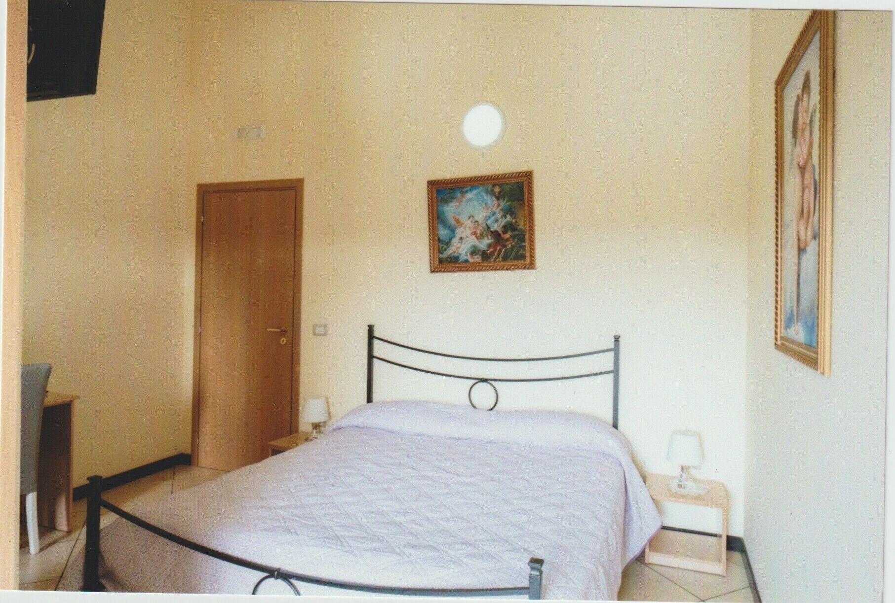 Een slaapkamer met een bed, nachtkastje, deur en een aan de muur hangend schilderij.